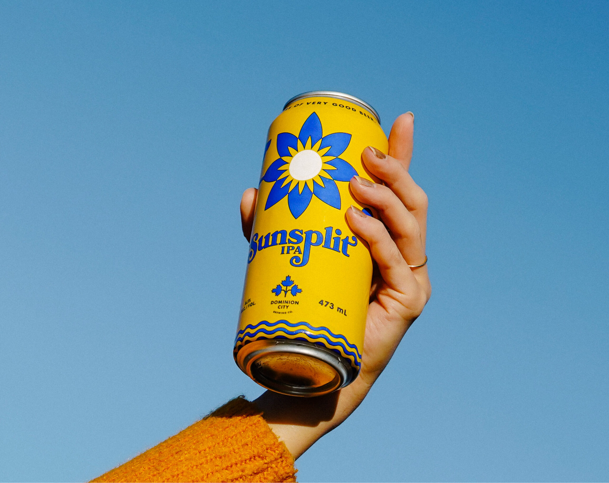 Hand holding a can of Dominion City's most popular beer, the iconic yellow and blue Sunsplit.